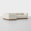 A modern, L-shaped sectional sofa with light beige fabric upholstery and a low, wooden base, set against a plain, light gray background.