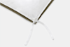 Close-up of the corner of a white comforter with a fabric tie, layered over an olive green bedsheet, on a light background.