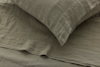 A close-up view of a pillow and bed sheet made from textured, olive-green linen fabric, neatly arranged on a bed.