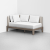 A minimalist daybed with a wooden frame, beige upholstered backrest, and three white pillows, placed in the corner of a white room with a light gray floor.
