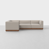 A modern L-shaped sectional sofa with light beige upholstery and a wooden base, set on a light gray floor against a plain white background.