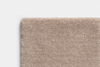 A close-up view of the corner of a beige, textured carpet with a soft, looped pile against a plain white background.