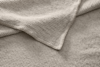 A close-up view of beige, textured waffle-knit fabric layers with visible stitching on the edges, creating a soft and cozy appearance.