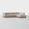 A modern L-shaped sectional sofa with light beige upholstery and a wooden base, placed on a plain light-colored floor against a white background.