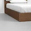 A close-up of a modern wooden bed frame with white bedding and a white pillow, set on a smooth, light gray floor.