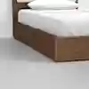 A close-up of a modern wooden bed frame with white bedding and a white pillow, set on a smooth, light gray floor.