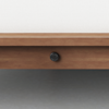 Close-up of a wooden furniture frame with a light-colored fabric panel above and a small round black knob centered on the wooden section. The background is a plain gray surface.
