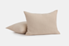 Two beige, textured throw pillows are placed on a plain white surface. One pillow is upright, while the other is lying flat behind it.