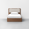A minimalist wooden bed with a light beige upholstered headboard, a single white pillow, and white bedding, placed against a plain white wall on a light gray floor.