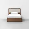 A minimalist wooden bed with a light beige upholstered headboard, a single white pillow, and white bedding, placed against a plain white wall on a light gray floor.