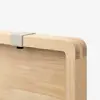 Close-up of a light wood cutting board with rounded edges, featuring a small metal clip attached to the top edge against a plain white background.