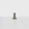 A small, rectangular wooden sculpture sits on a flat, light gray concrete surface against a plain white background. The design features stepped layers, creating a minimalist, geometric look.