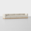 A modern, light beige sectional sofa with a low wooden base, featuring four connected seats and squared armrests, set against a plain light gray background.