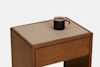 A dark coffee mug with a red handle sits on top of a wooden side table with a beige surface against a plain white background.