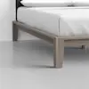 Close-up of the corner of a light wood bed frame with white bedding, showing clean lines and modern design on a smooth, light gray floor.