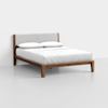 A modern wooden bed frame with angled legs, a light gray upholstered headboard, and a white mattress with two white pillows, set against a plain white wall and floor.