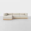 A modern, L-shaped sectional sofa with light beige upholstery and a light wooden base, set against a plain white background on a smooth, light gray floor.