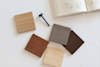 Four wood samples in different shades are arranged on a white surface near a black screw and an open sketchbook with technical drawings.