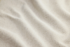 Close-up of a textured, off-white fabric with small, looped fibers and gentle, wavy folds, creating a soft and cozy appearance.