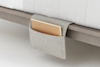 A gray felt bedside caddy is hanging over the edge of a bed frame, holding a brown spiral notebook in its pocket.