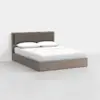A modern platform bed with a light wood frame and a padded, taupe upholstered headboard, made up with white sheets, pillows, and a duvet; set against a plain white wall and floor.