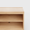 A close-up view of a light wood cabinet with an open shelf and a minimalist design, shown against a plain white background.