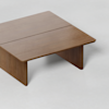 A square wooden coffee table with a simple, modern design, featuring clean lines and a smooth surface, positioned on a light-colored floor.