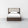A modern twin bed with a dark wood frame, light beige upholstered headboard, and white bedding, centered against a plain white wall on a light gray floor.