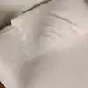 A neatly made bed with a white fitted sheet, a beige pillow, and a matching beige duvet, set against a textured brown headboard.