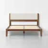 A wooden bed frame with a light beige upholstered headboard, slatted base, and minimalist design, set against a plain white wall on a gray floor.