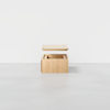 A light wooden storage box with a detached lid hovering above it, displayed against a plain white background on a smooth gray floor.