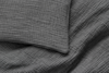 A close-up view of a dark gray, textured blanket and pillow with a crinkled, grid-like pattern on soft fabric.