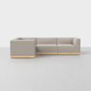 A modern L-shaped sectional sofa with light grey upholstery and a light wood base, set on a smooth light grey floor against a plain white background.