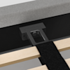 Close-up of a bed frame assembly showing a black metal support bracket attached to wooden slats, with a black fabric strap and part of a gray mattress visible above.
