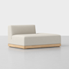 A modern, minimalist beige chaise lounge with a low backrest and wooden base, placed on a light gray floor against a plain white background.