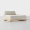 A modern, minimalist beige chaise lounge with a low backrest and wooden base, placed on a light gray floor against a plain white background.