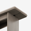 Close-up view of the corner of a light wood table, showing the tabletop and leg with smooth, rounded edges and a visible screw connecting the two pieces. The background is plain white.