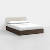 A modern bed with a dark wooden frame, white mattress, white bedding, two white pillows, and a light beige upholstered headboard, set against a plain white background.