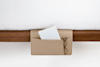 A beige felt bedside organizer hangs from a wooden bed frame, holding a white journal and a pair of eyeglasses. A white comforter covers the bed above.