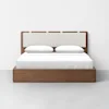 A modern wooden bed with a rectangular upholstered headboard, white bedding, and two white pillows, set against a plain white wall and gray floor.
