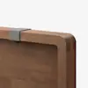 Close-up of a wooden tabletop with rounded edges, featuring a small, gray metal or plastic clamp attached to the top edge against a plain white background.