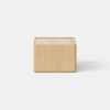 A minimalist, light wood nightstand with a single drawer partially open, placed on a plain, light-colored surface against a white background.