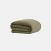 A neatly folded olive green blanket or quilt is displayed against a plain, light gray background.