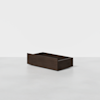 A rectangular, dark wood storage drawer sits on a light gray surface against a white background. The drawer is empty and has no handles or visible hardware.