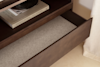 An open wooden drawer with a light gray lining, beneath a shelf holding a book titled Portraits of Home | DISC Interiors. The drawer is empty, and soft natural light filters through a nearby curtain.