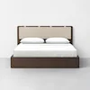 A modern bed with a dark wooden frame and beige upholstered headboard, neatly made with white bedding and two white pillows, set against a plain white wall and light gray floor.