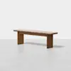 A minimalist wooden bench with a rectangular seat and two sturdy, flat legs. The wood has a warm, medium-brown finish and the bench is set against a plain white background.