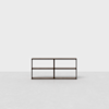 A minimalist, dark wood shelving unit with four open compartments, placed against a plain white wall on a light gray floor.