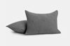 Two gray rectangular pillows with a subtle textured pattern, placed on a light gray background; one pillow is upright while the other lies flat behind it.