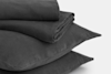 Two dark gray pillows stacked on top of each other with a matching folded duvet or blanket placed neatly on top, set against a plain light background.